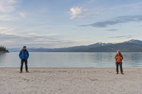 Original: two hikers stand far apart beside a lake.